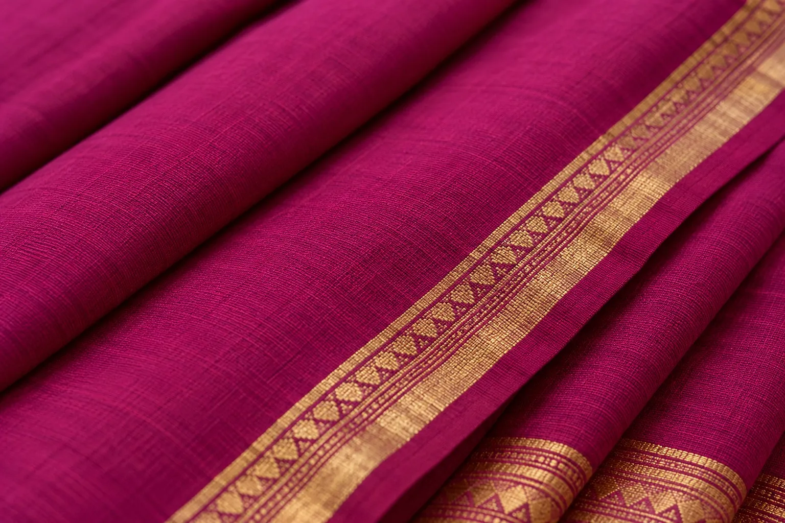 Close-up of a pressed magenta cotton saree with a woven gold-coloured border